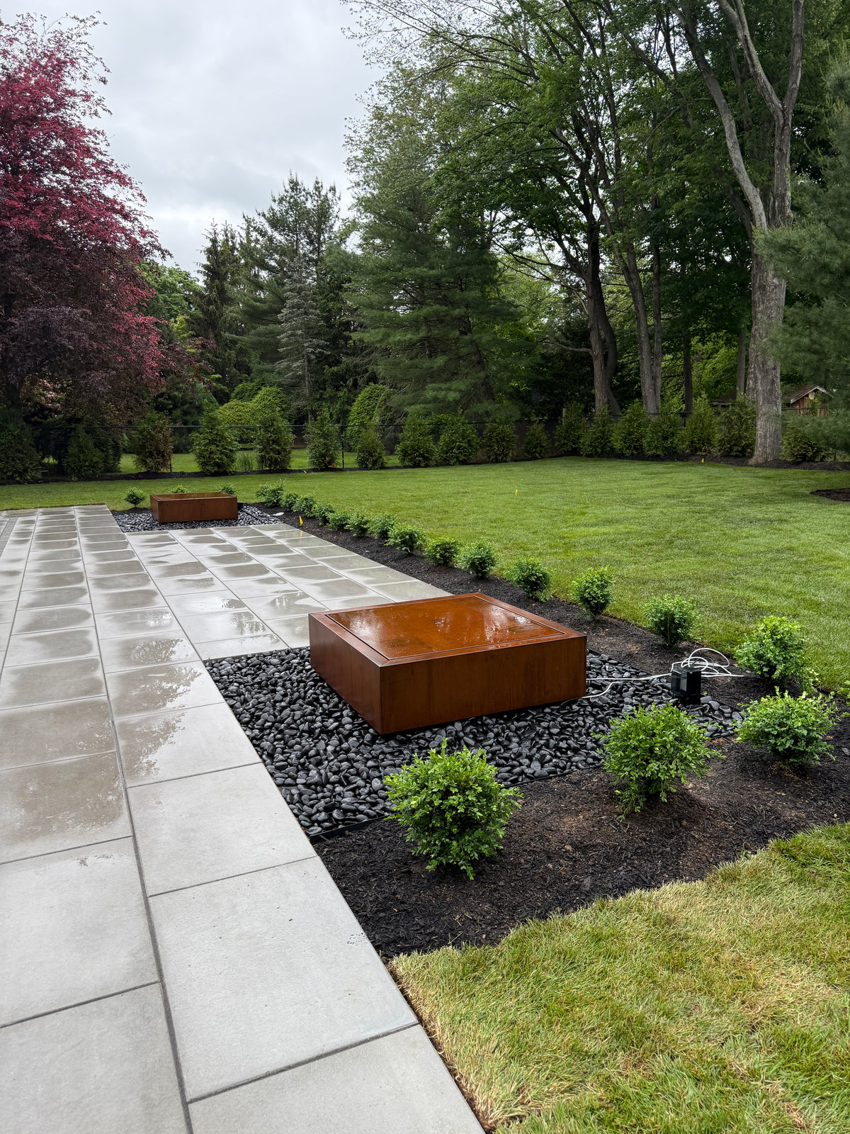Two matching square Corten steel fountains set in black river stone beds along a modern paver patio, customer photo