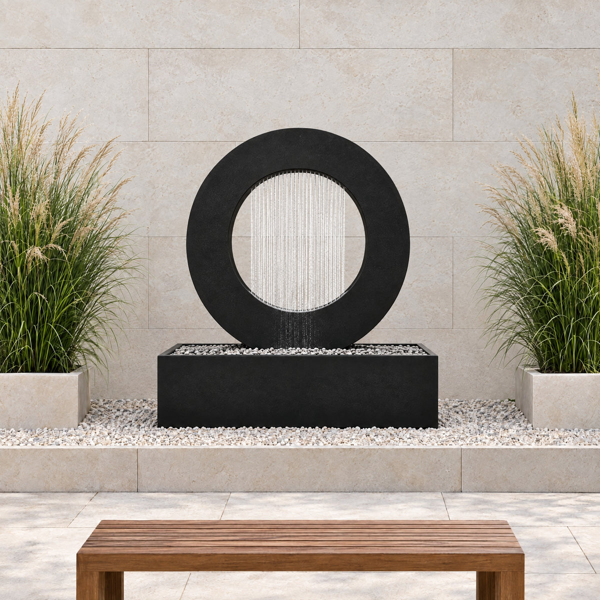 Black steel Halo rain curtain fountain in a gravel bed against a limestone wall with ornamental grasses