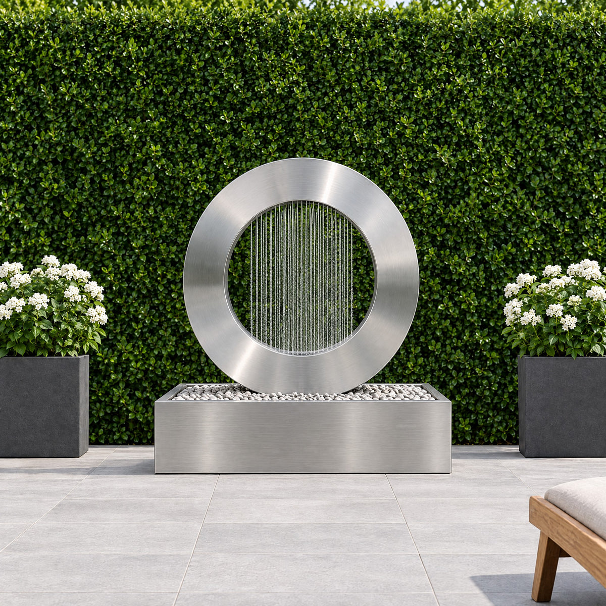 Stainless steel Halo rain curtain fountain on a modern terrace in front of a green hedge wall