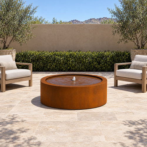 Corten steel Mesa Circular fountain centered on a stone terrace between two lounge chairs
