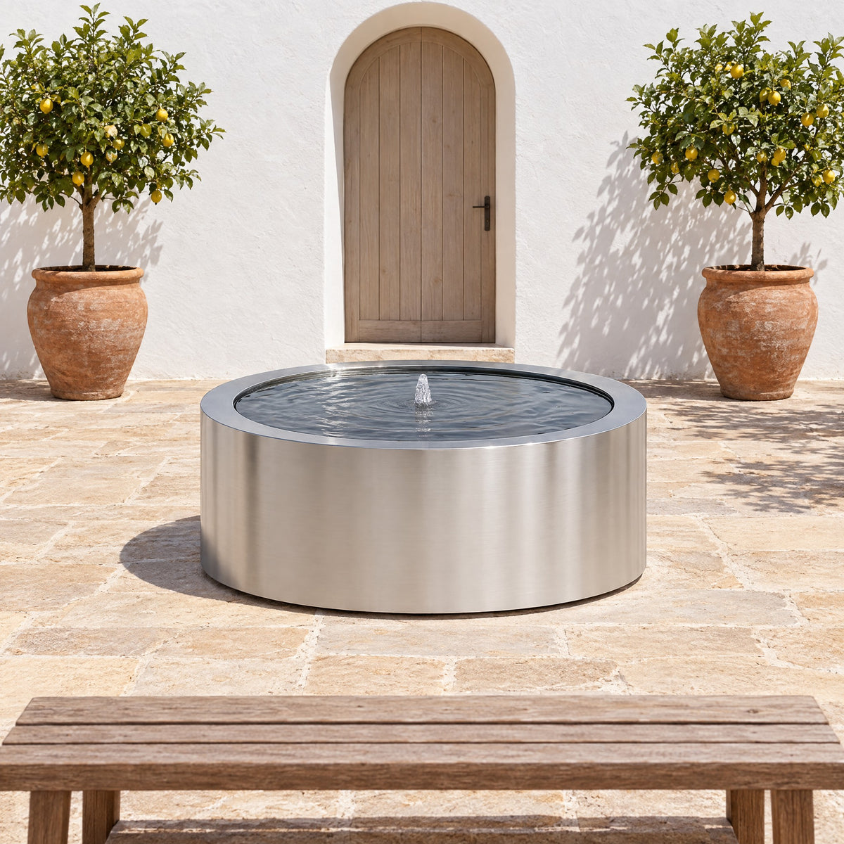 Stainless steel Mesa Circular fountain in a whitewashed courtyard with citrus trees and an arched door