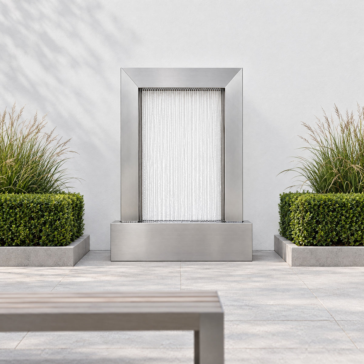 Serenity Frame stainless steel rain curtain fountain centered on a white courtyard wall between boxwood beds
