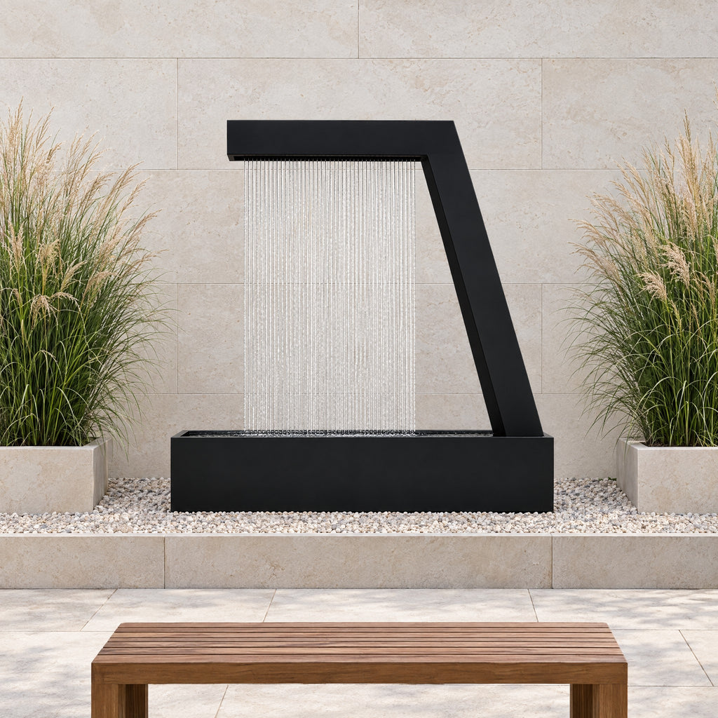 Black steel Zura Flow rain curtain fountain in a gravel bed against a limestone wall with ornamental grasses